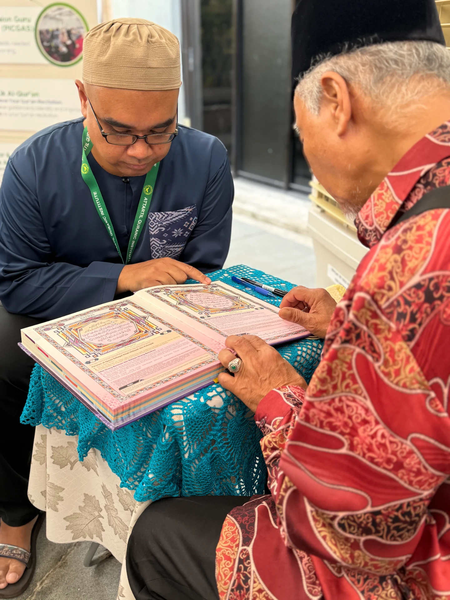 A teacher reading an illuminated Qur'an with an elderly visitor