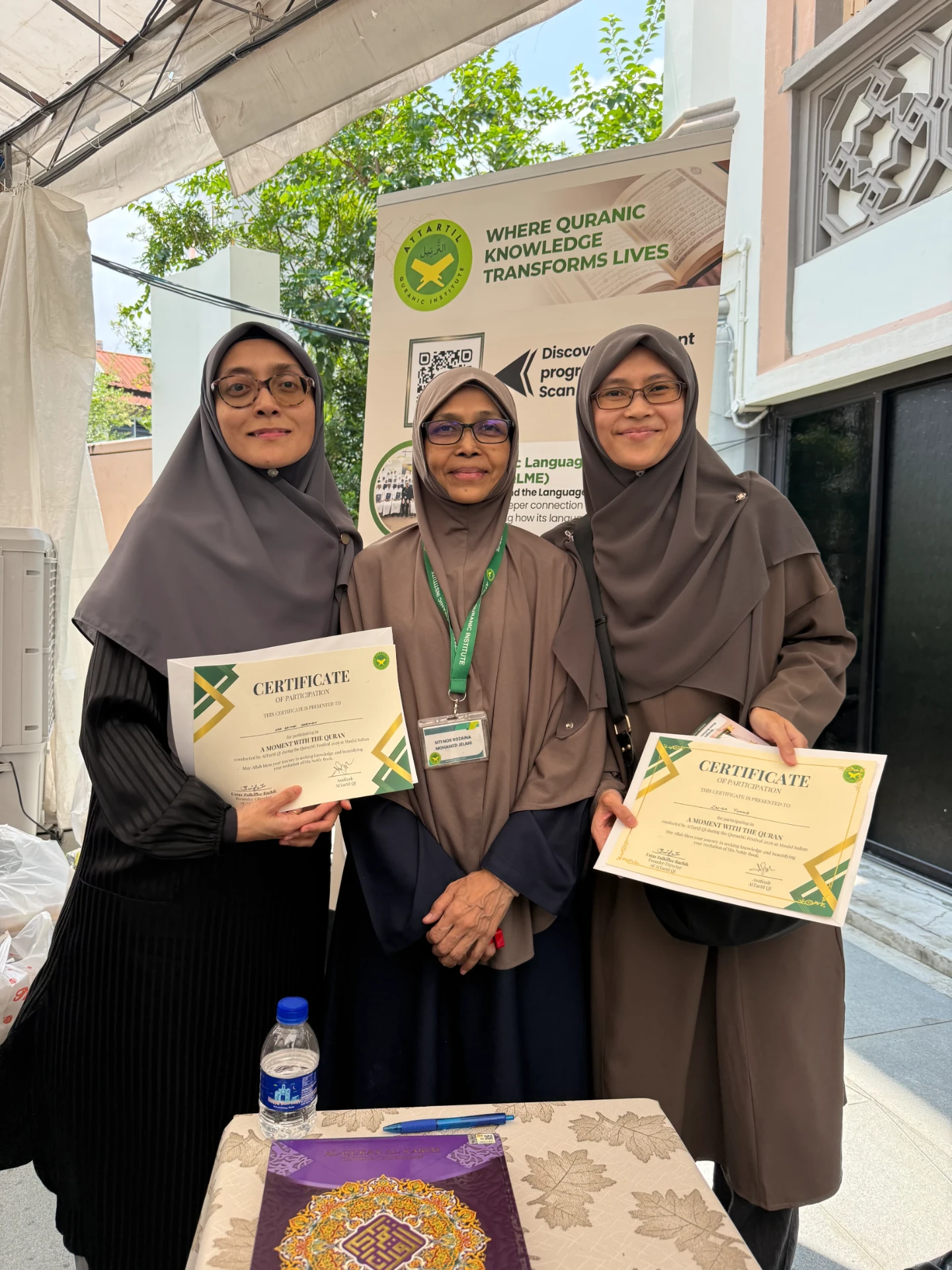 Participants holding their 'A Moment With Al-Quran' certificates at the AtTartil QI booth