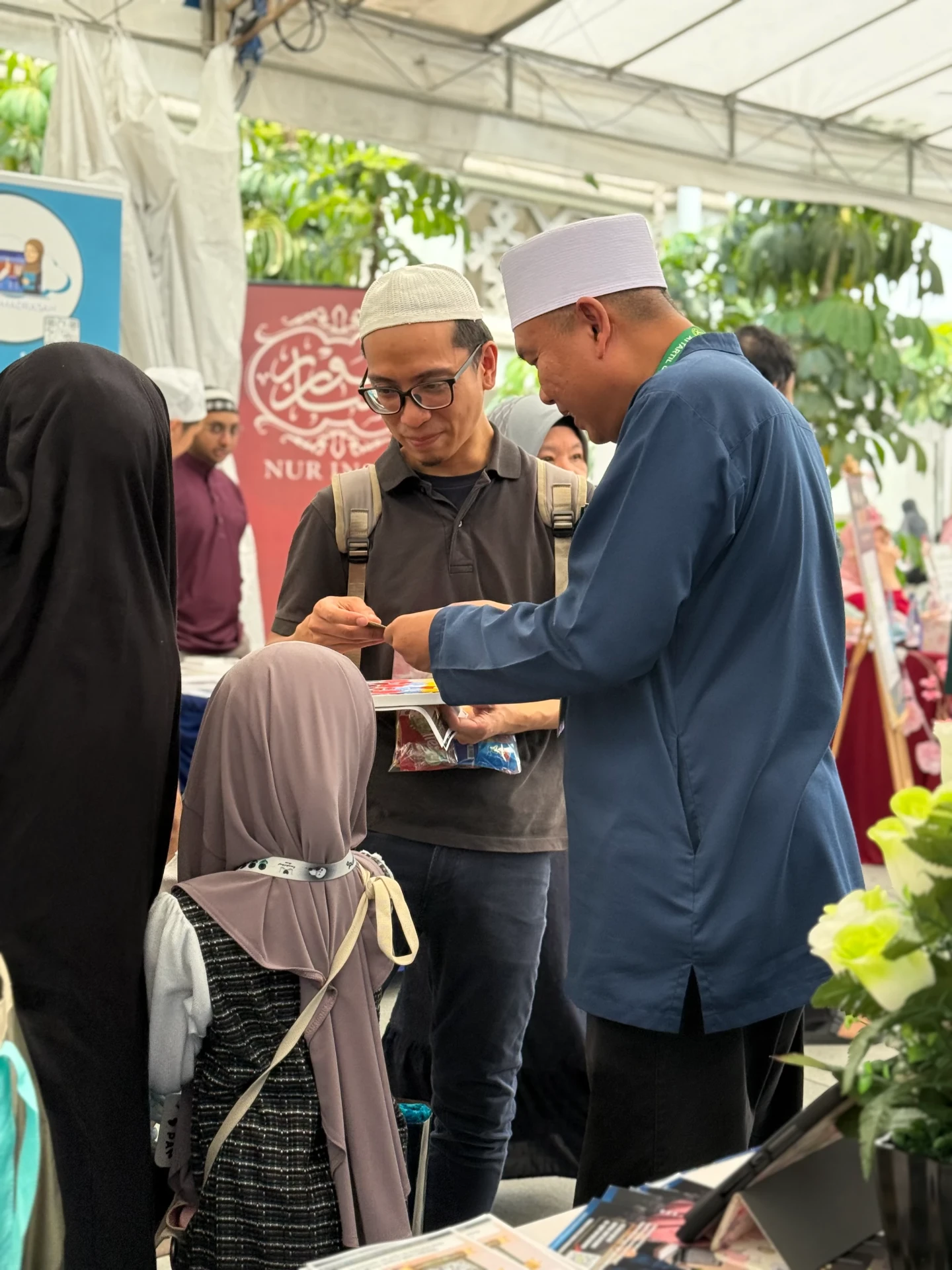 An AtTartil QI teacher guiding a visitor and his child at the booth