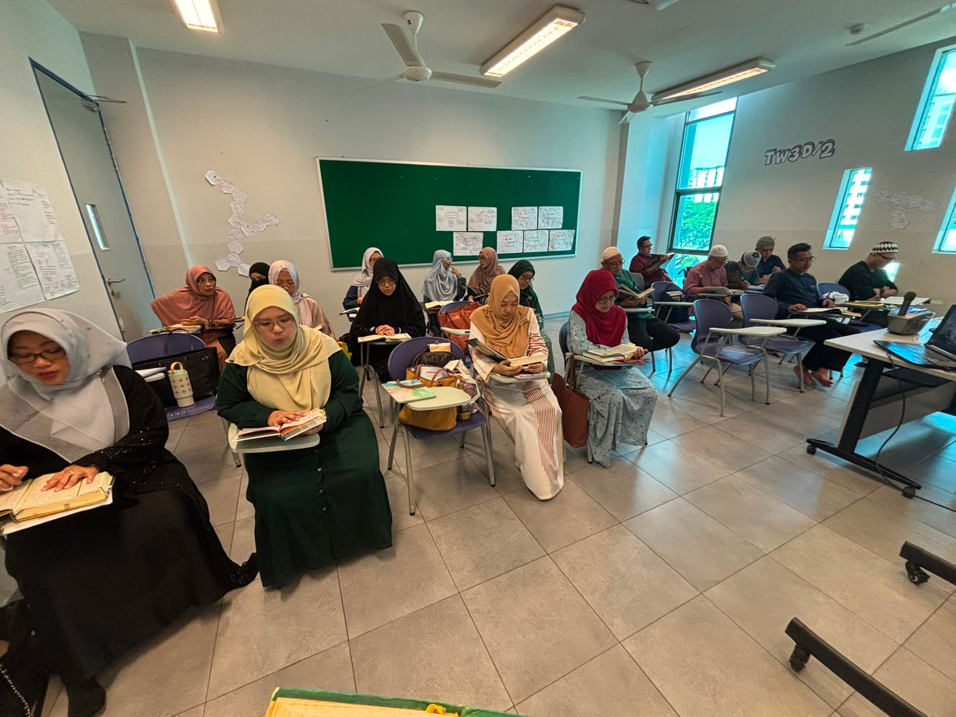 A small group of adult Muslim learners reading the Qur'an together with a teacher in a bright Singapore classroom