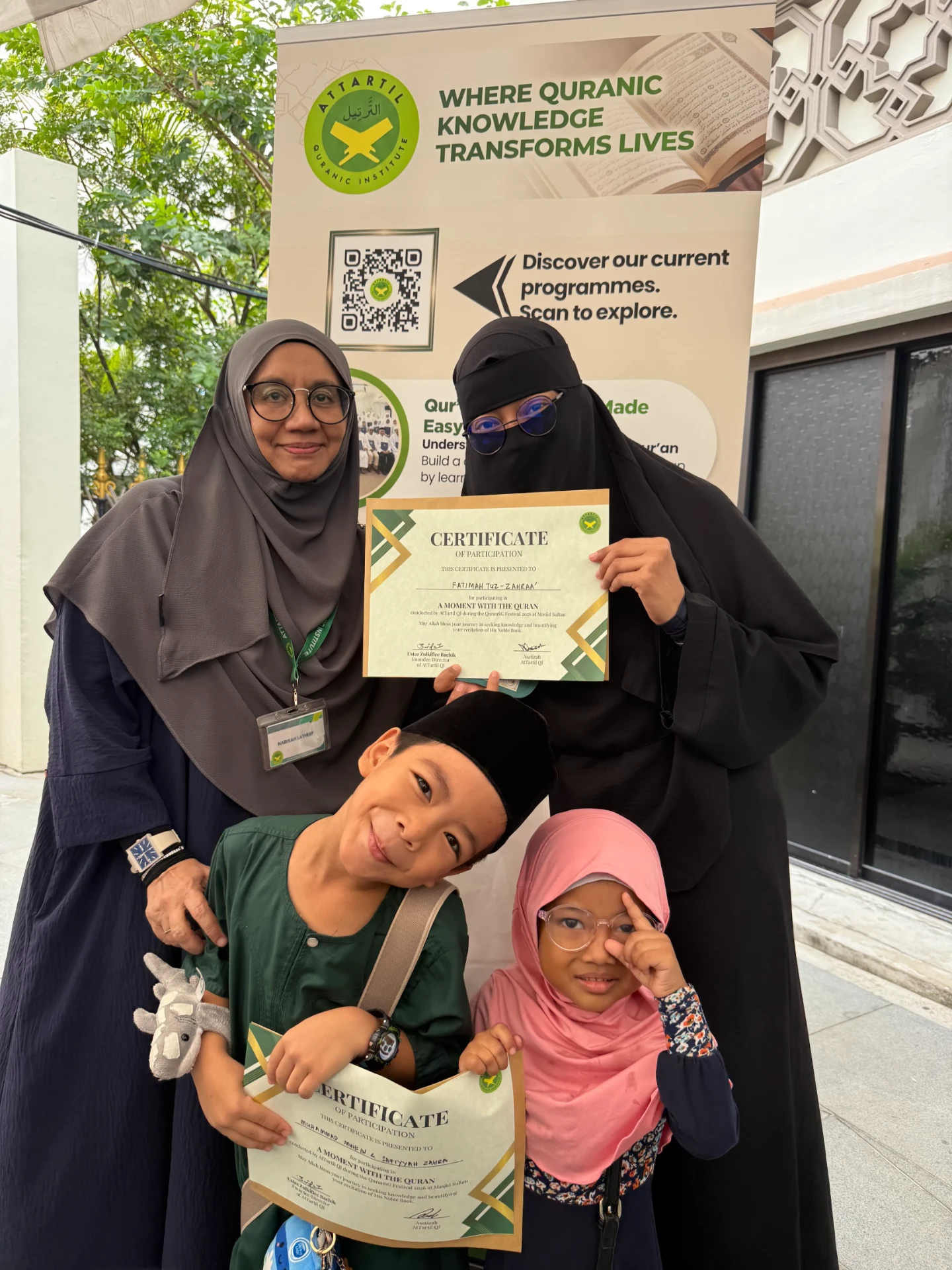 A family holding their 'A Moment With The Quran' certificates at the booth