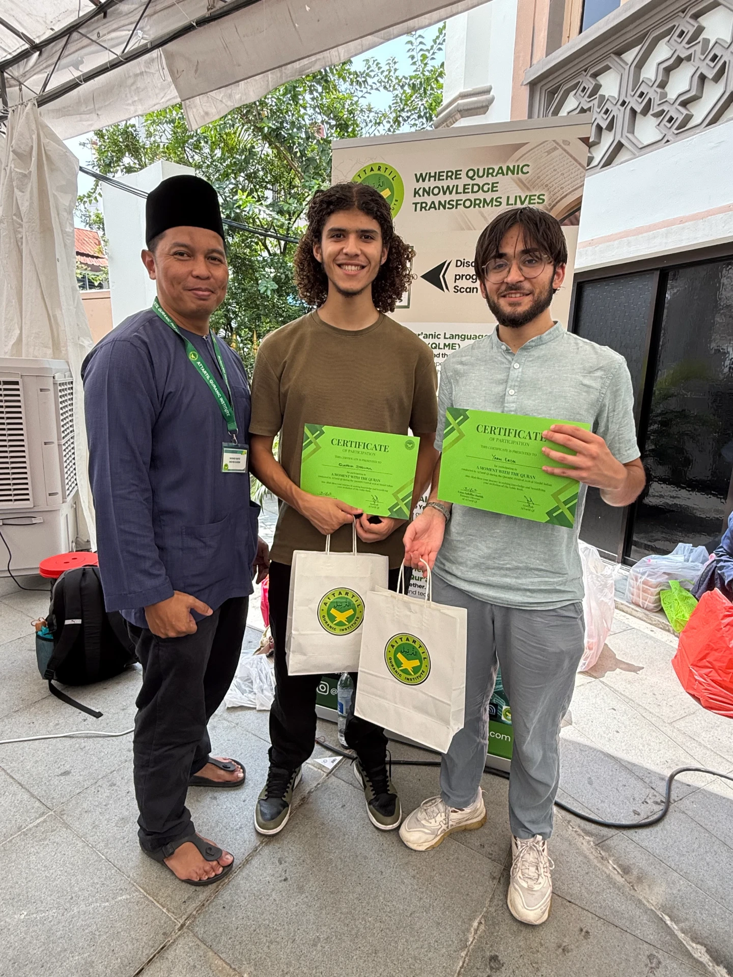 Two international visitors with their certificates and AtTartil QI goodie bags