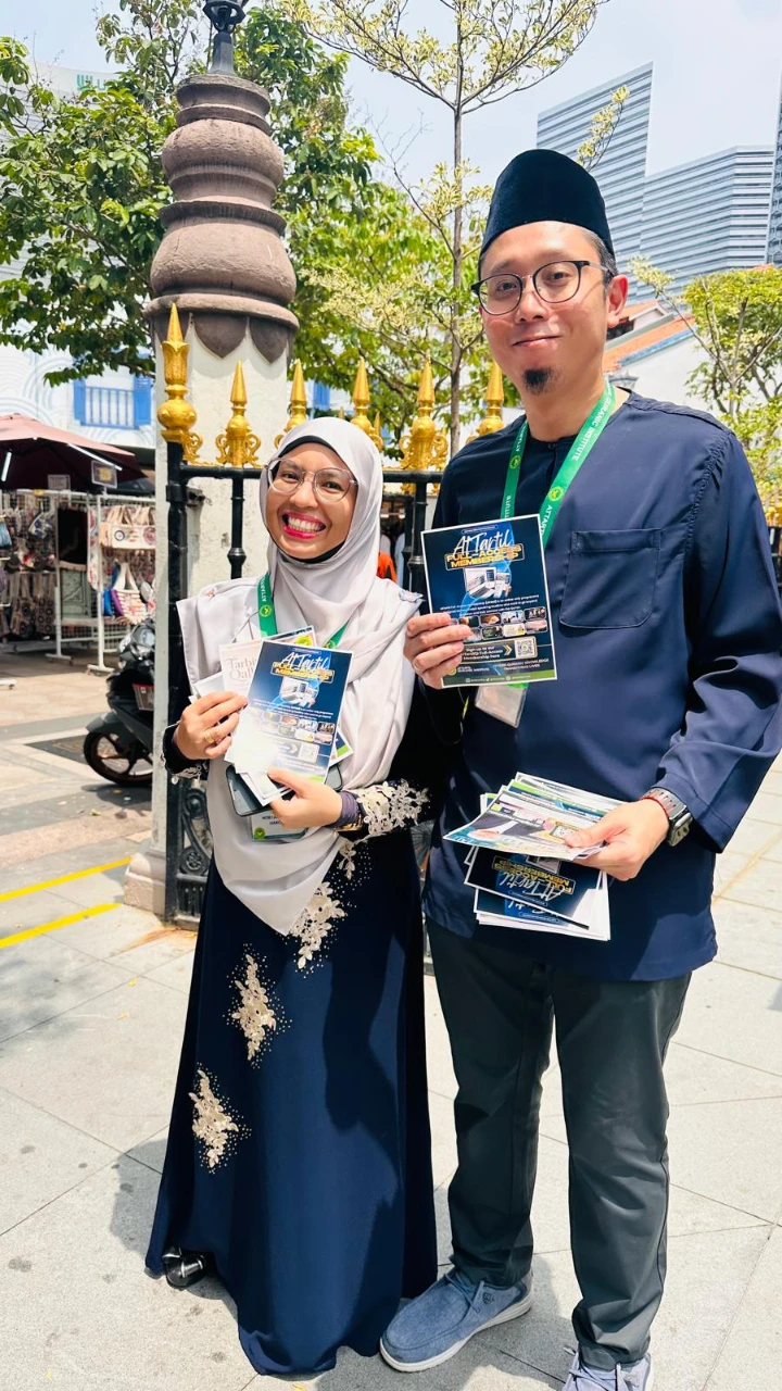Two AtTartil QI volunteers holding programme flyers outside Masjid Sultan