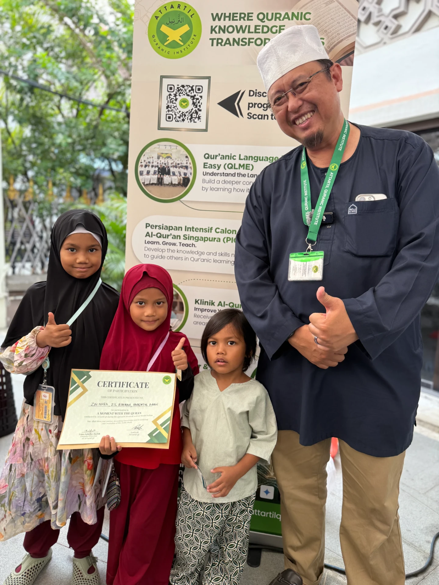 Three young girls holding their certificate with Ustaz Zulkiflee at the booth