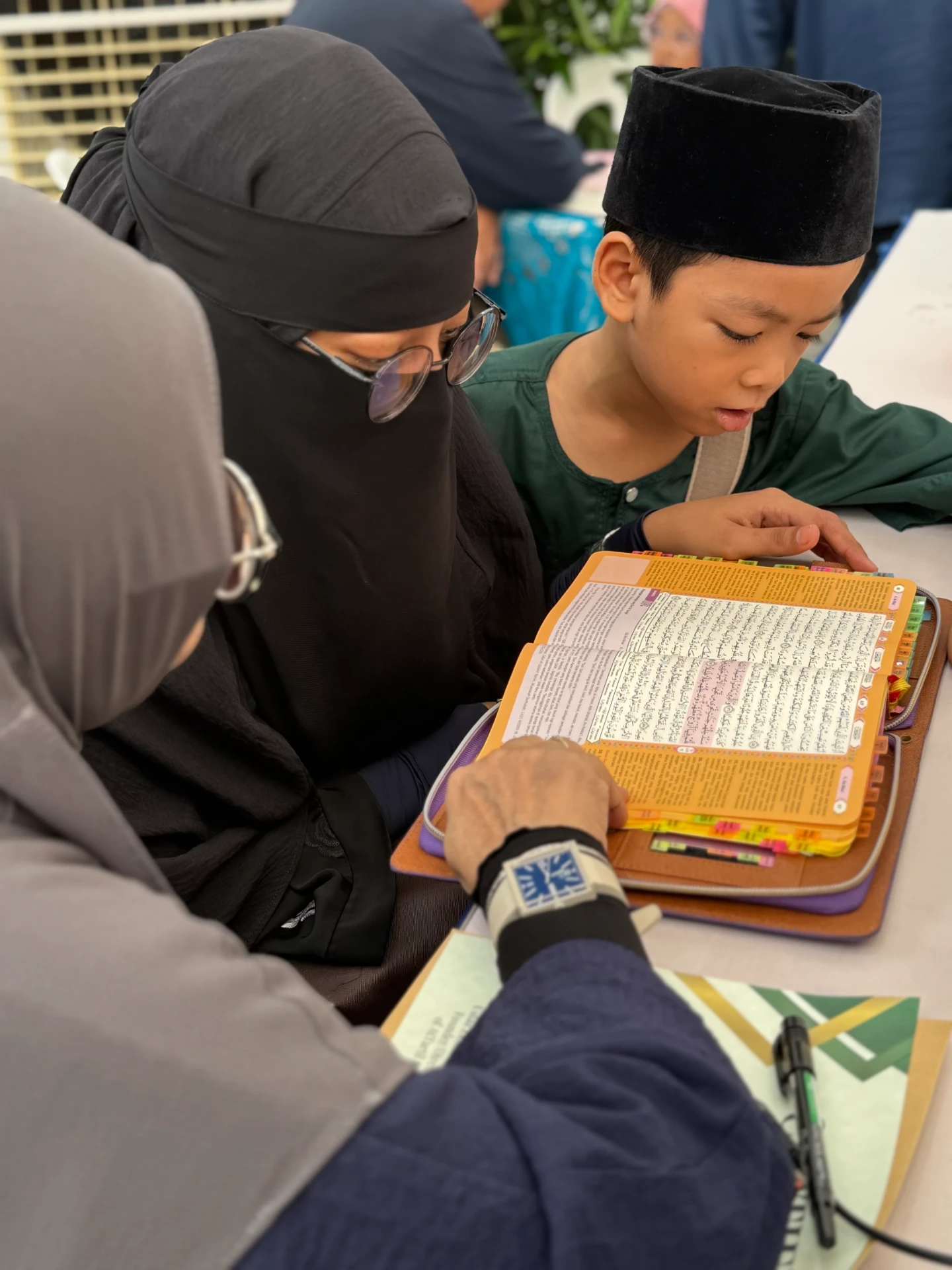 A young boy reciting the Qur'an with teachers guiding him