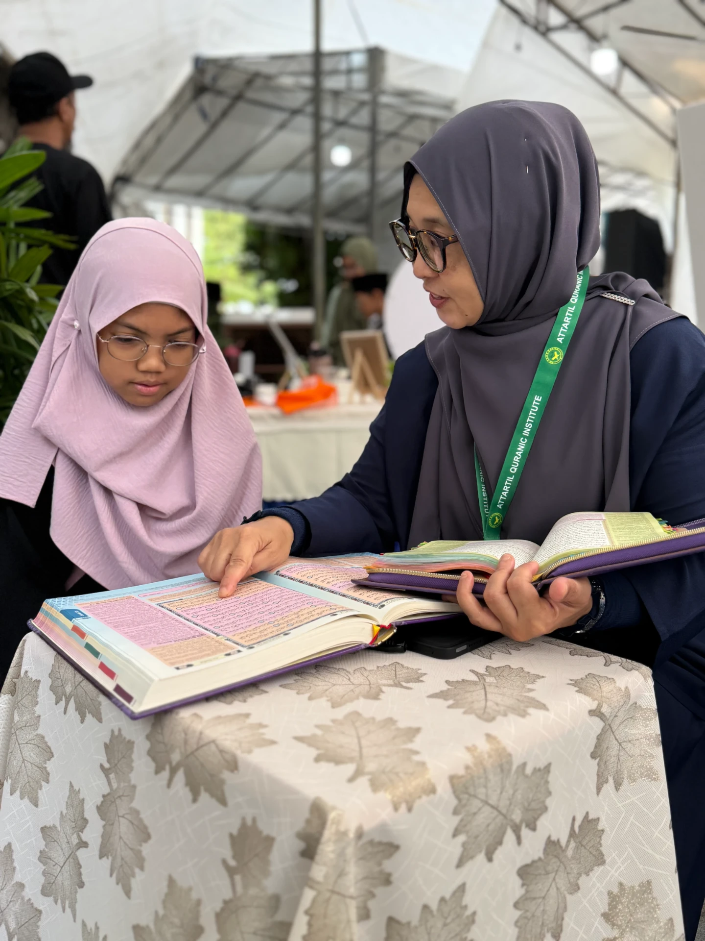 A teacher guiding a young girl through a page of the Qur'an