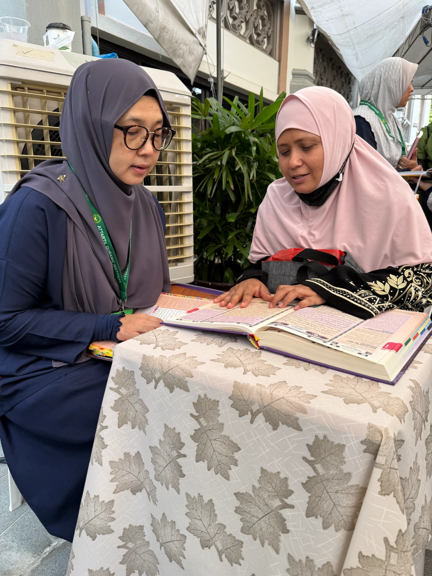 Two women reading the Qur'an together at the AtTartil QI booth