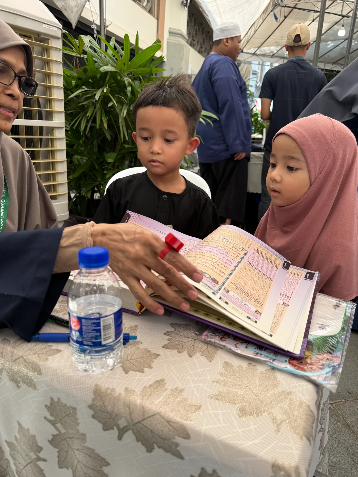 A teacher guiding two young children through a page of the Qur'an